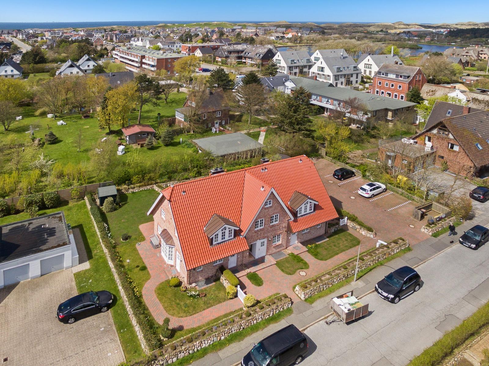 Haus mit rotem Dach und Garten. Mehrere Autos auf dem Hof. Blick auf die Ortschaft und das Meer.