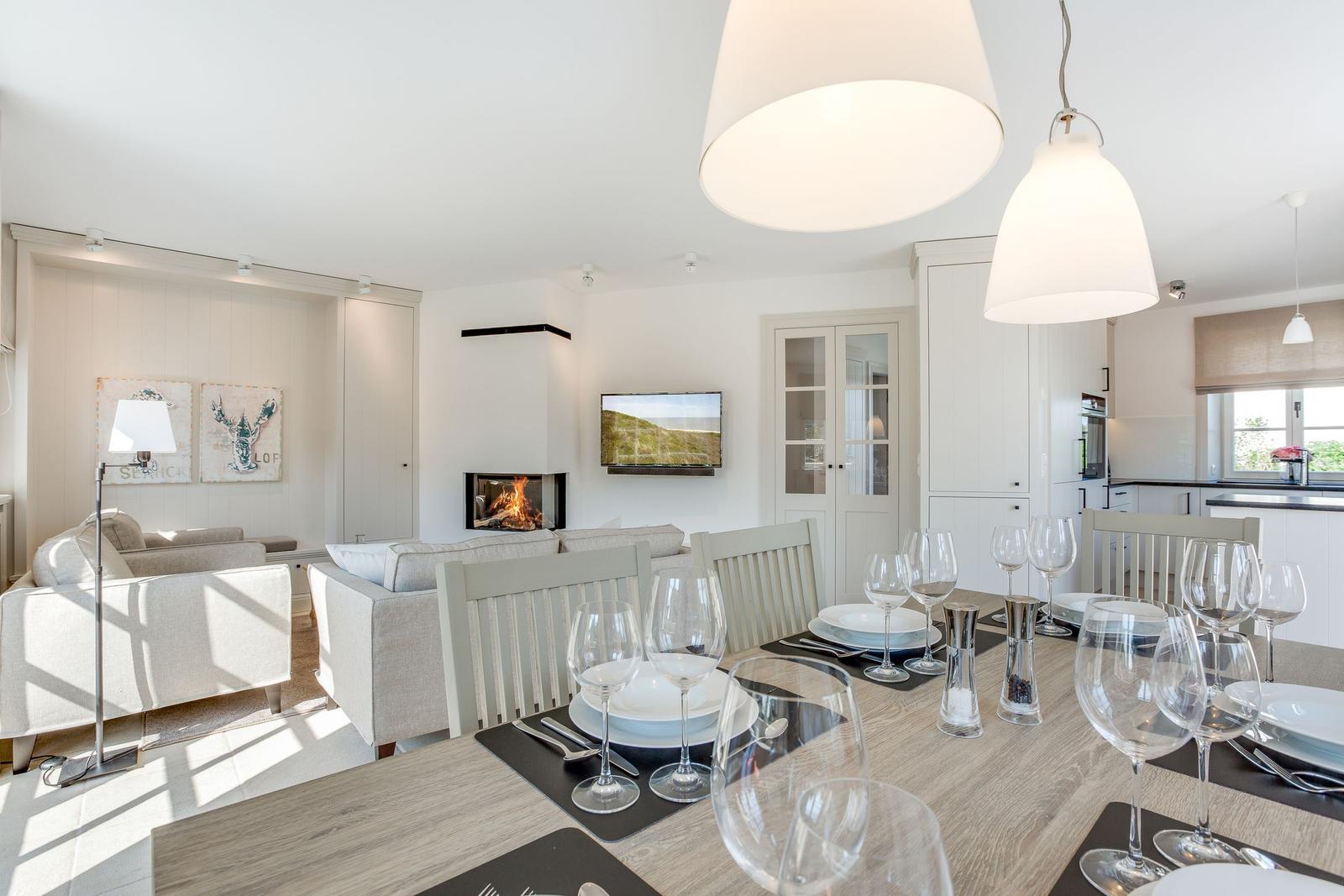 Essbereich mit Tisch und Stühlen, Wohnbereich mit Sofa und Kamin, Küche im Hintergrund.