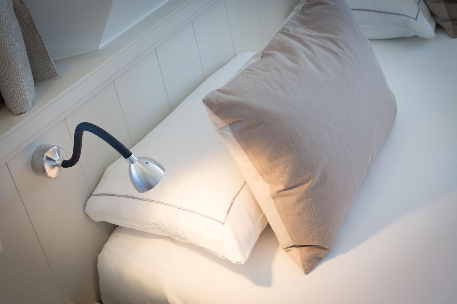Bettkopfteil mit Kissen und Wandlampe.