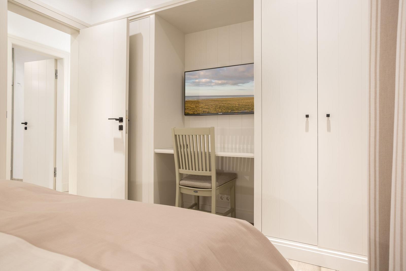 Schlafzimmer mit Schreibtisch, Stuhl und Fernseher an der Wand.