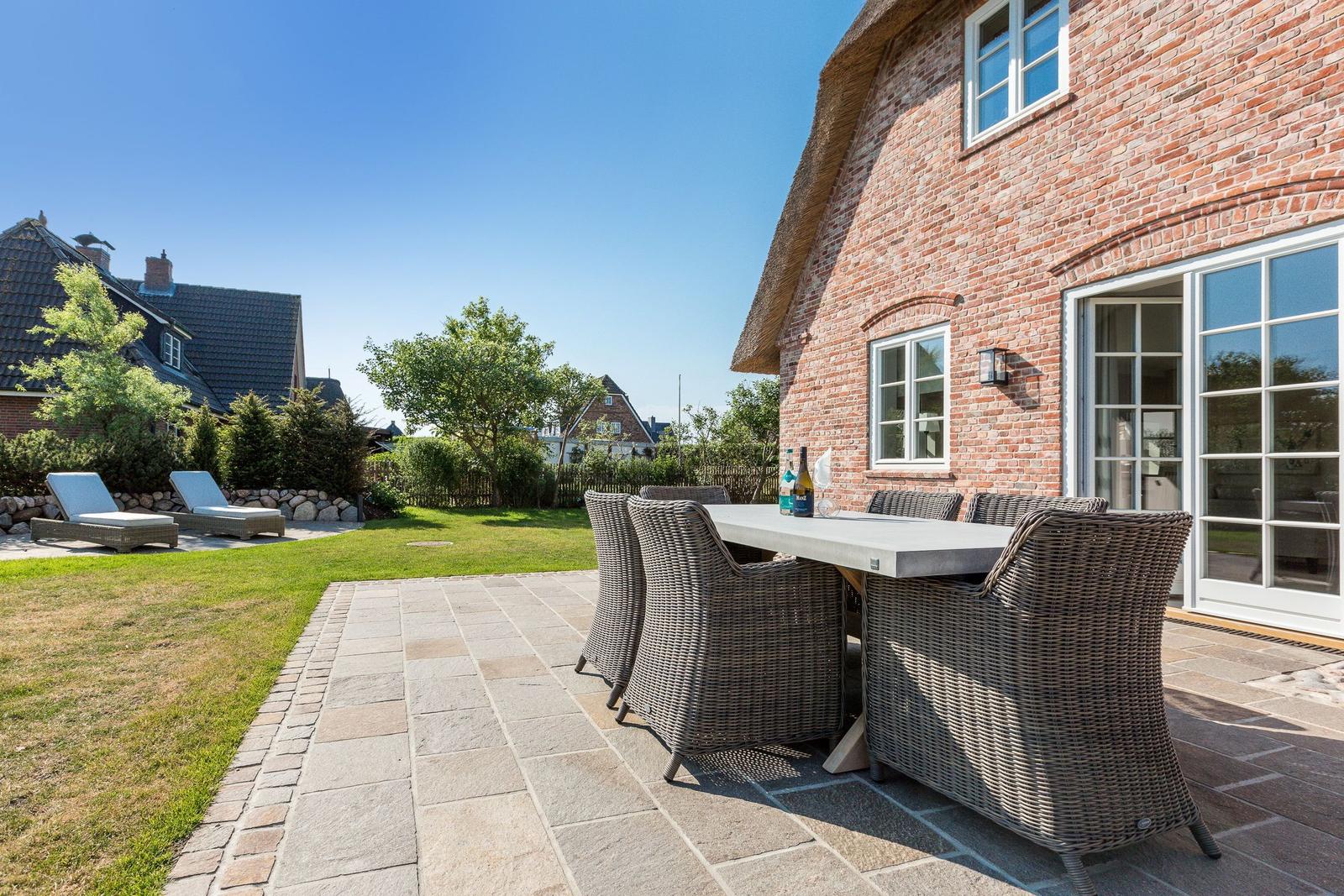 Terrasse mit Esstisch und Stühlen neben einem Backsteinhaus mit Schiebetür.