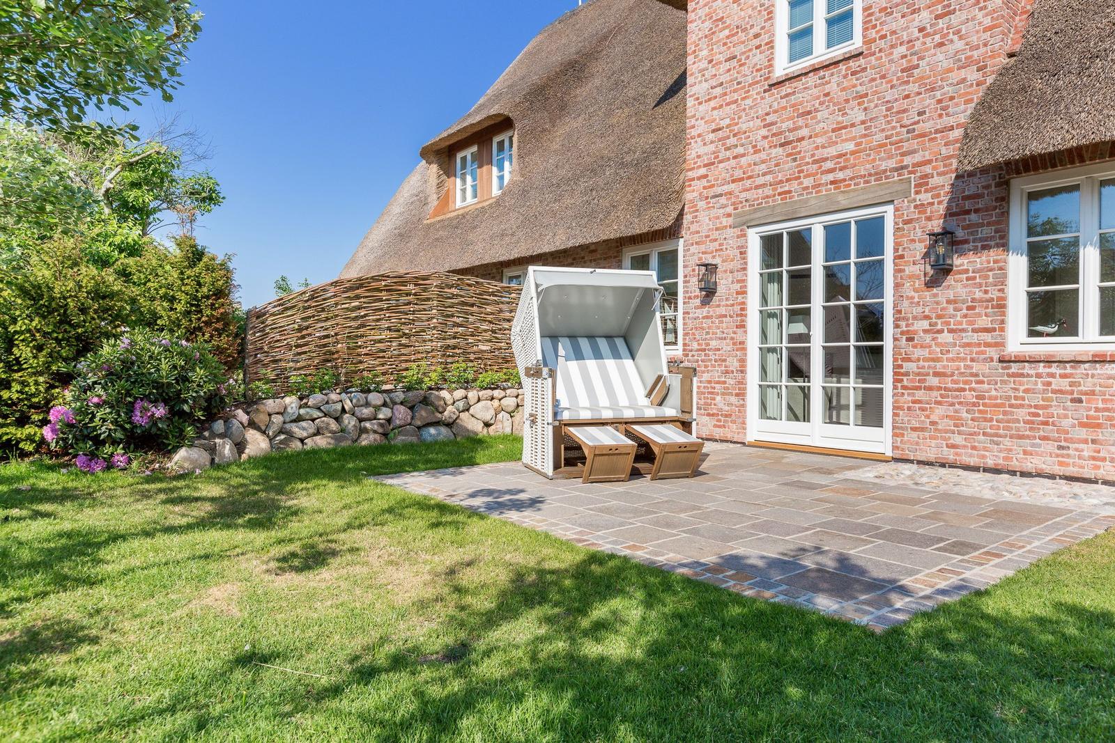 Haus mit strohgedecktem Dach und Steinmauer im Garten mit Liegestuhl.