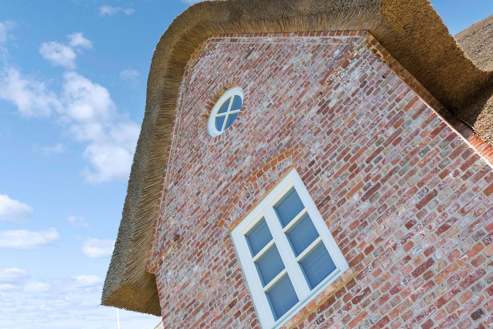 Rotes Ziegelhaus mit Strohdach und Fenstern unter blauem Himmel.
