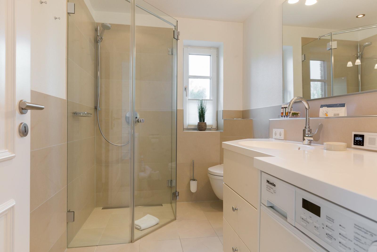 Bathroom with shower, sink, and toilet. Integrated Miele washing machine.