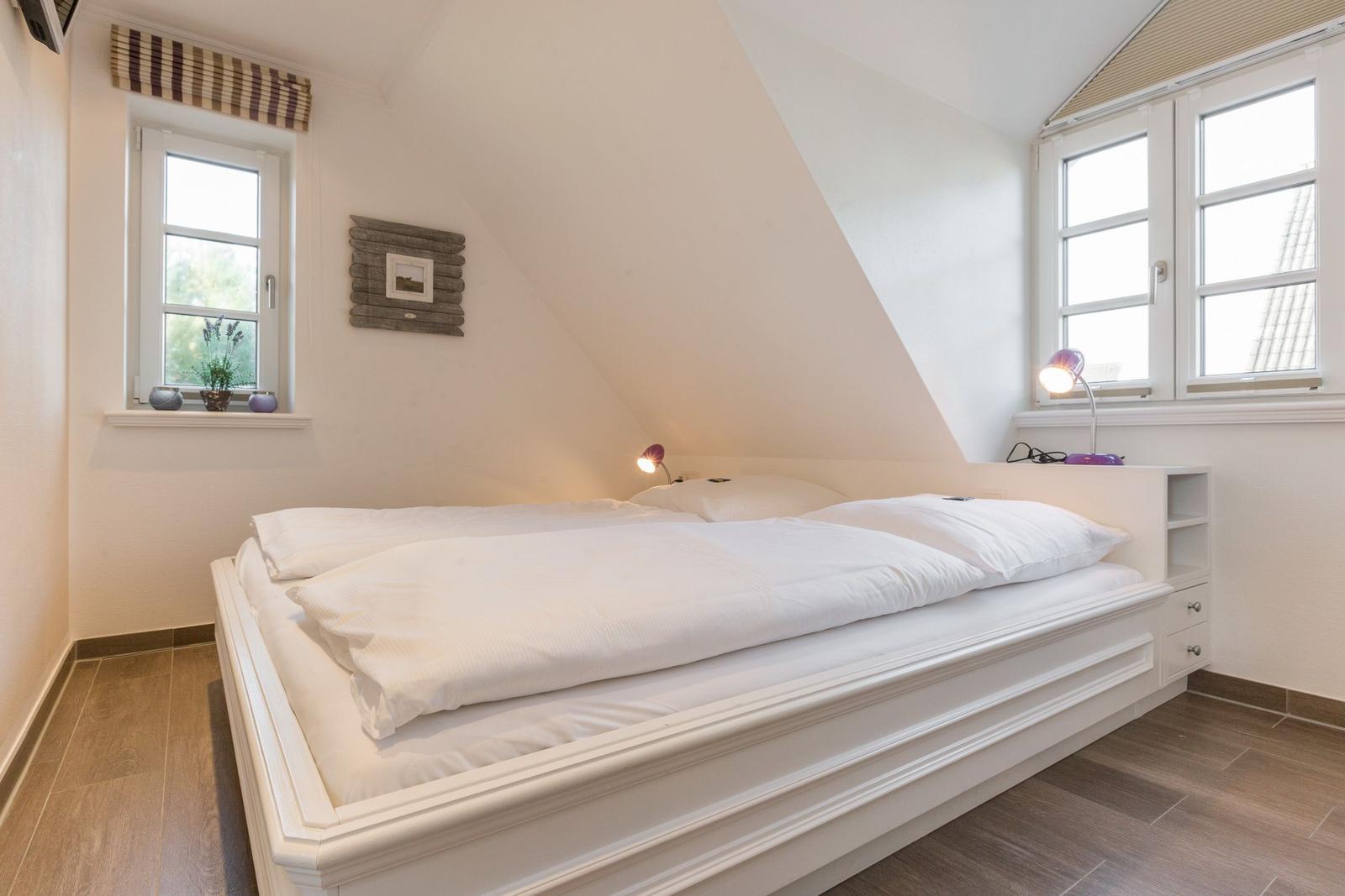 Bedroom with double bed, two windows, and wooden floor.