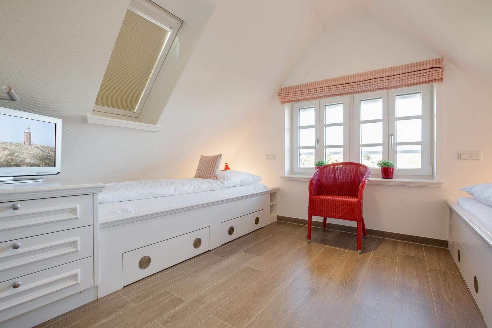 Bedroom with sloped ceiling, bed, TV, and red seating.