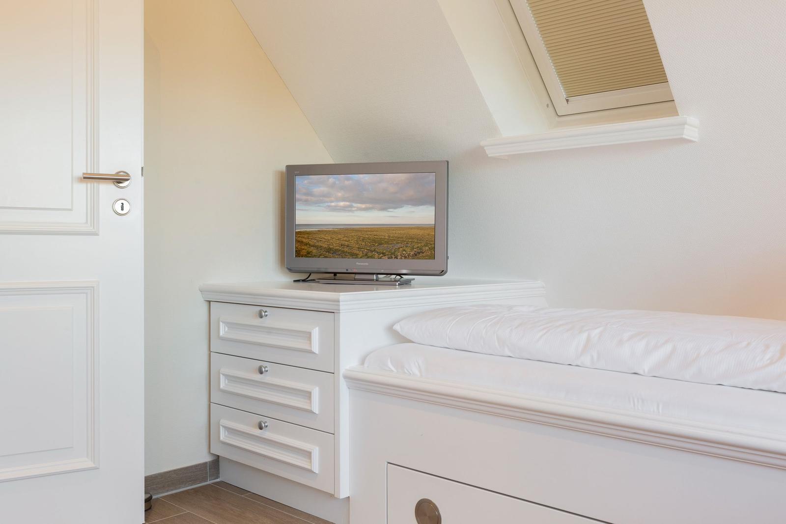 Bedroom with bed, dresser, and TV under sloped ceiling.