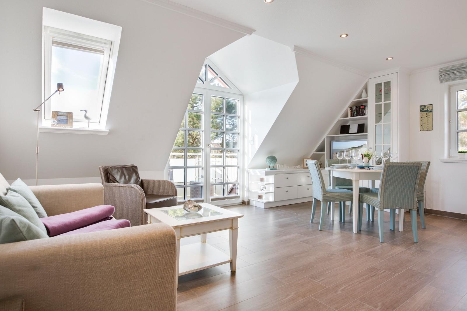 Living and dining area with sloped ceilings, glass doors, and wooden floor.