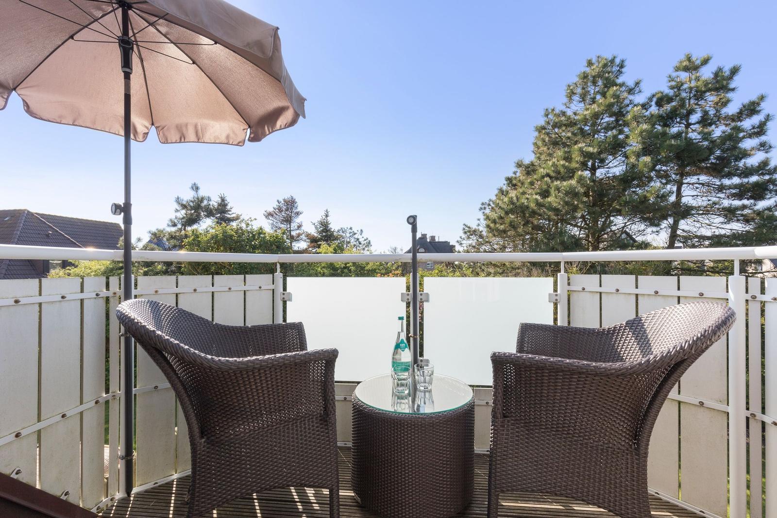 Terrace with two chairs, table, and umbrella. View of trees and sky.