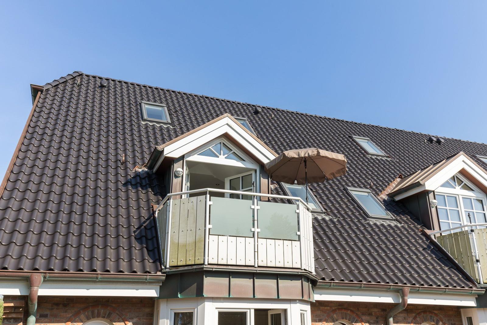 Attic level with balcony and umbrella under blue sky.