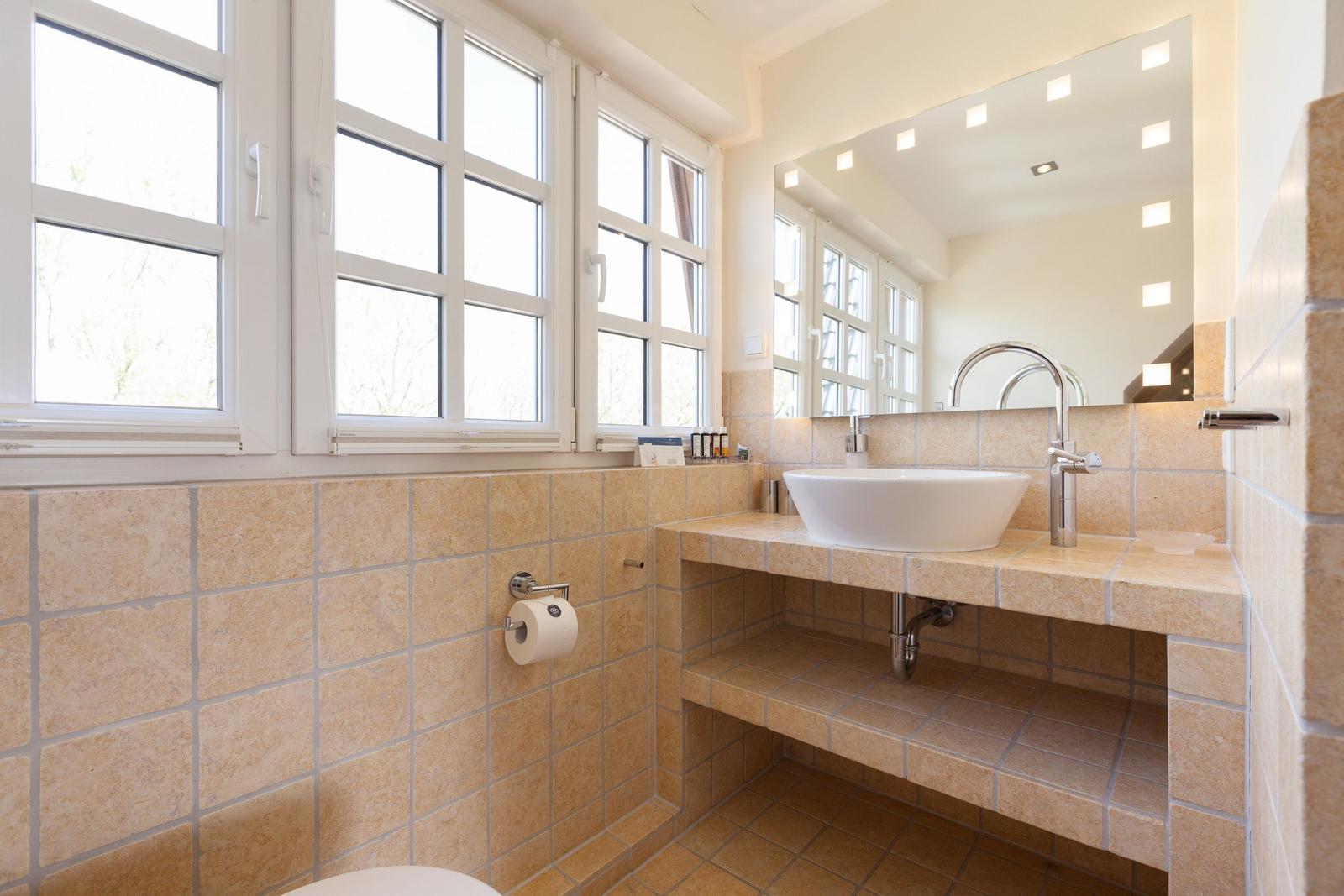 Badezimmer mit Waschbecken, Spiegel und Fenstern