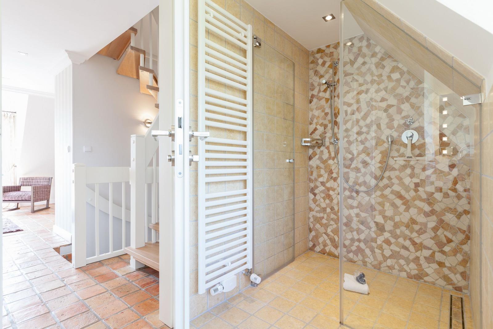 Dusche mit Mosaikwand, Heizkörper und angrenzender Treppe.