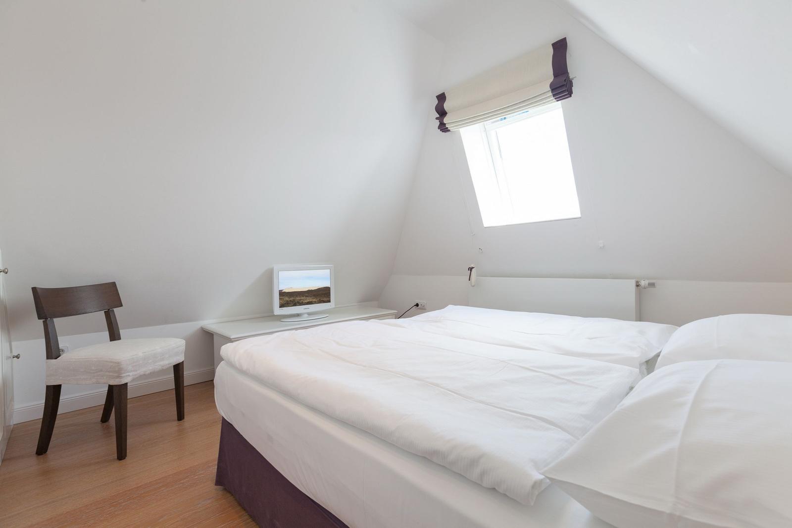Schlafzimmer mit Doppelbett, Stuhl und Fenster unter Dachschräge.