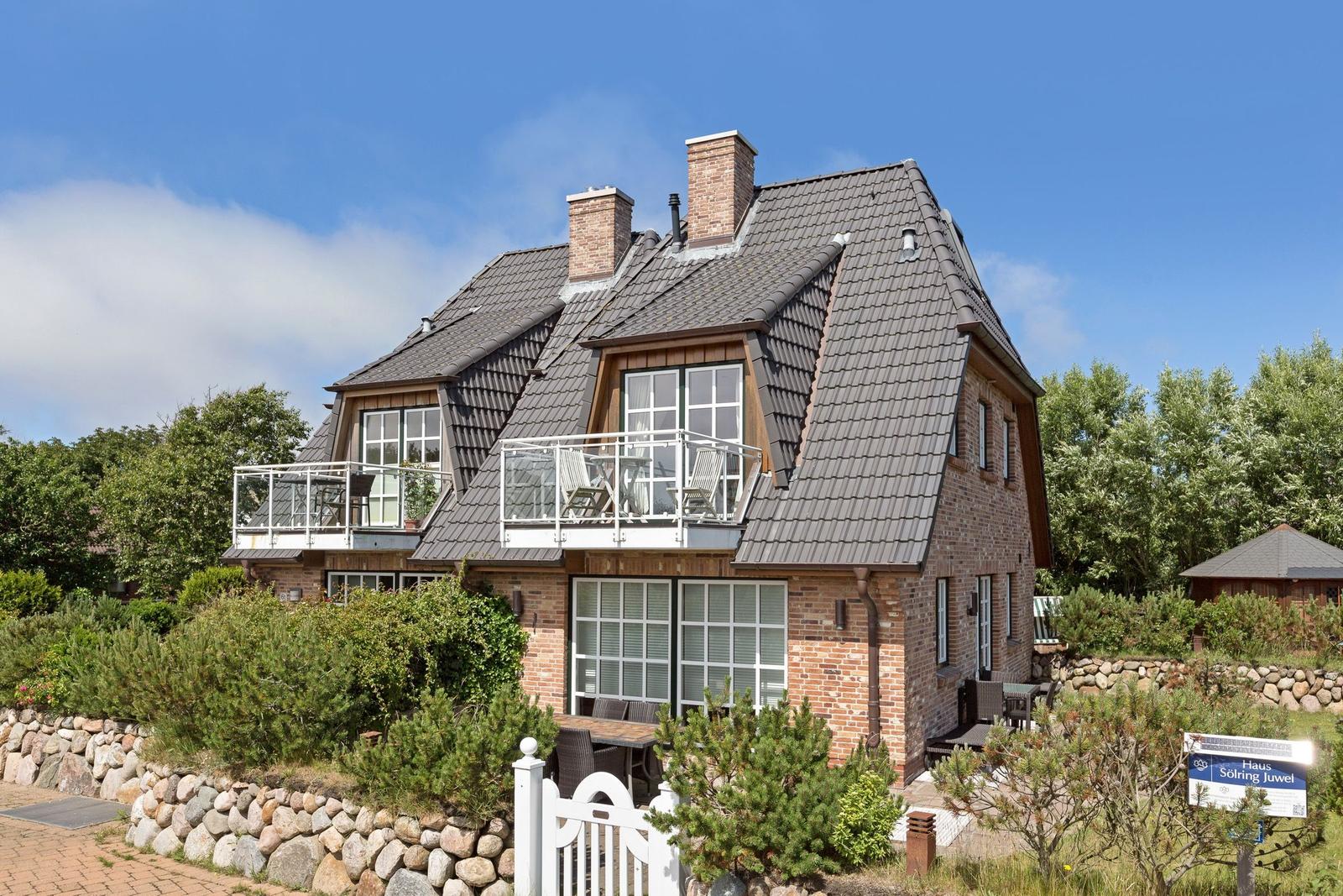 Haus mit Balkon, Terrasse und Garten. Steinmauer und weiße Zaun.