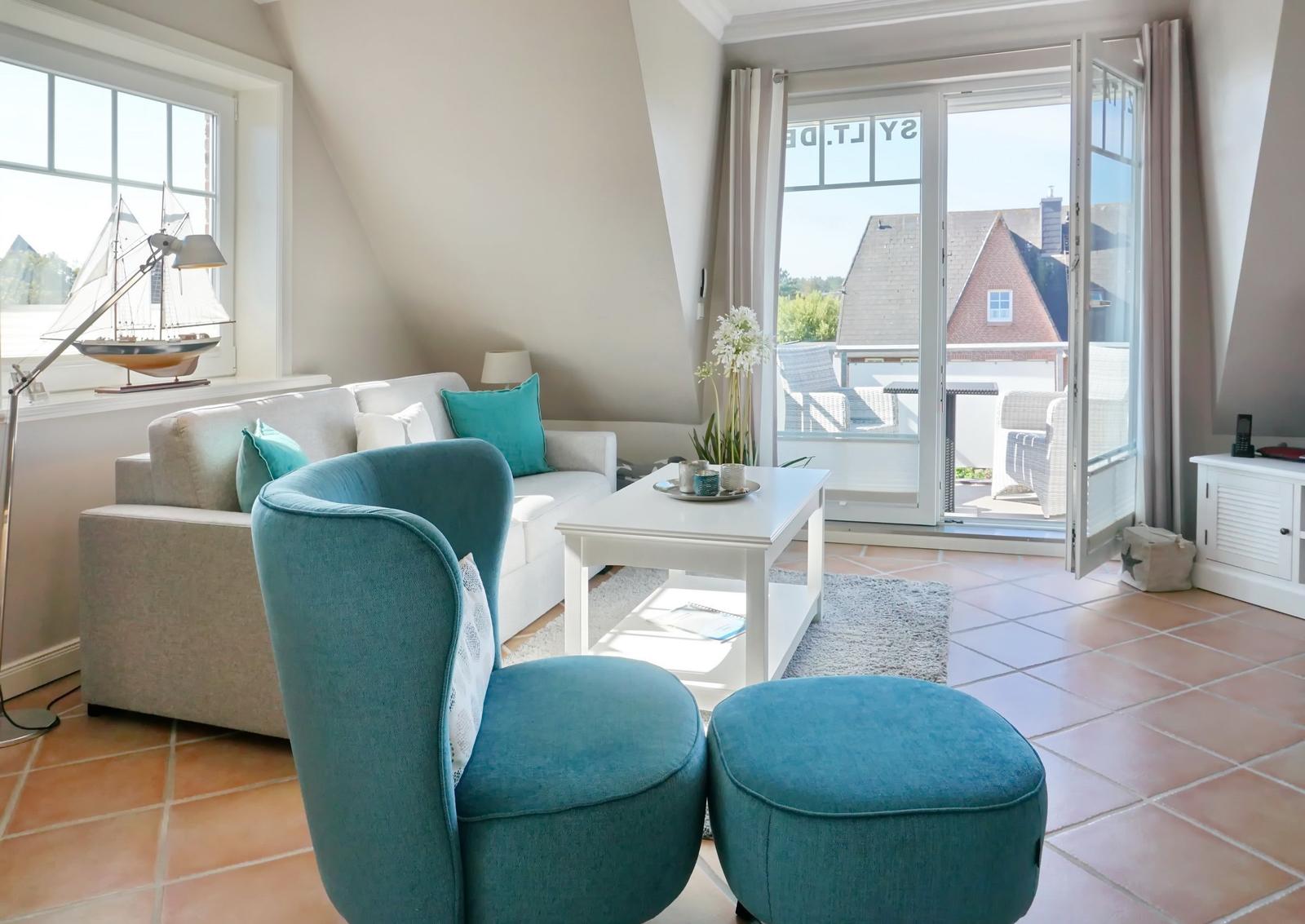 Wohnzimmer mit Sofa, blauem Sessel und Terrasse. Blick auf Dächer und Garten.