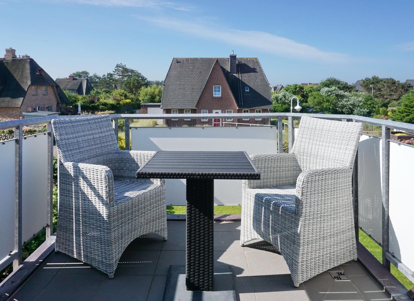 Terrasse mit zwei Stühlen und Tisch. Blick auf Häuser und Grünflächen.