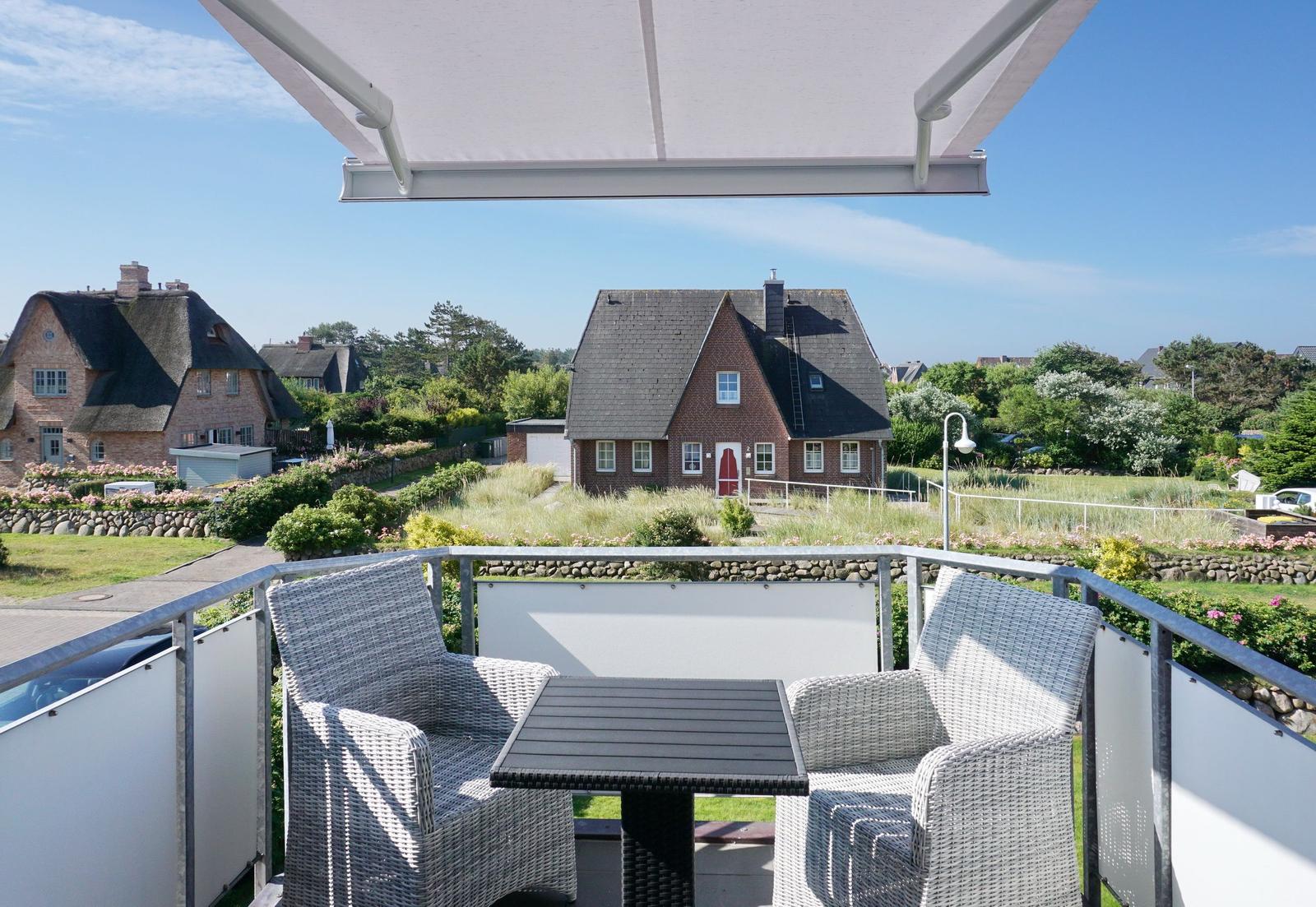 Terrasse mit Tisch und Stühlen. Blick auf Häuser und Grünflächen.
