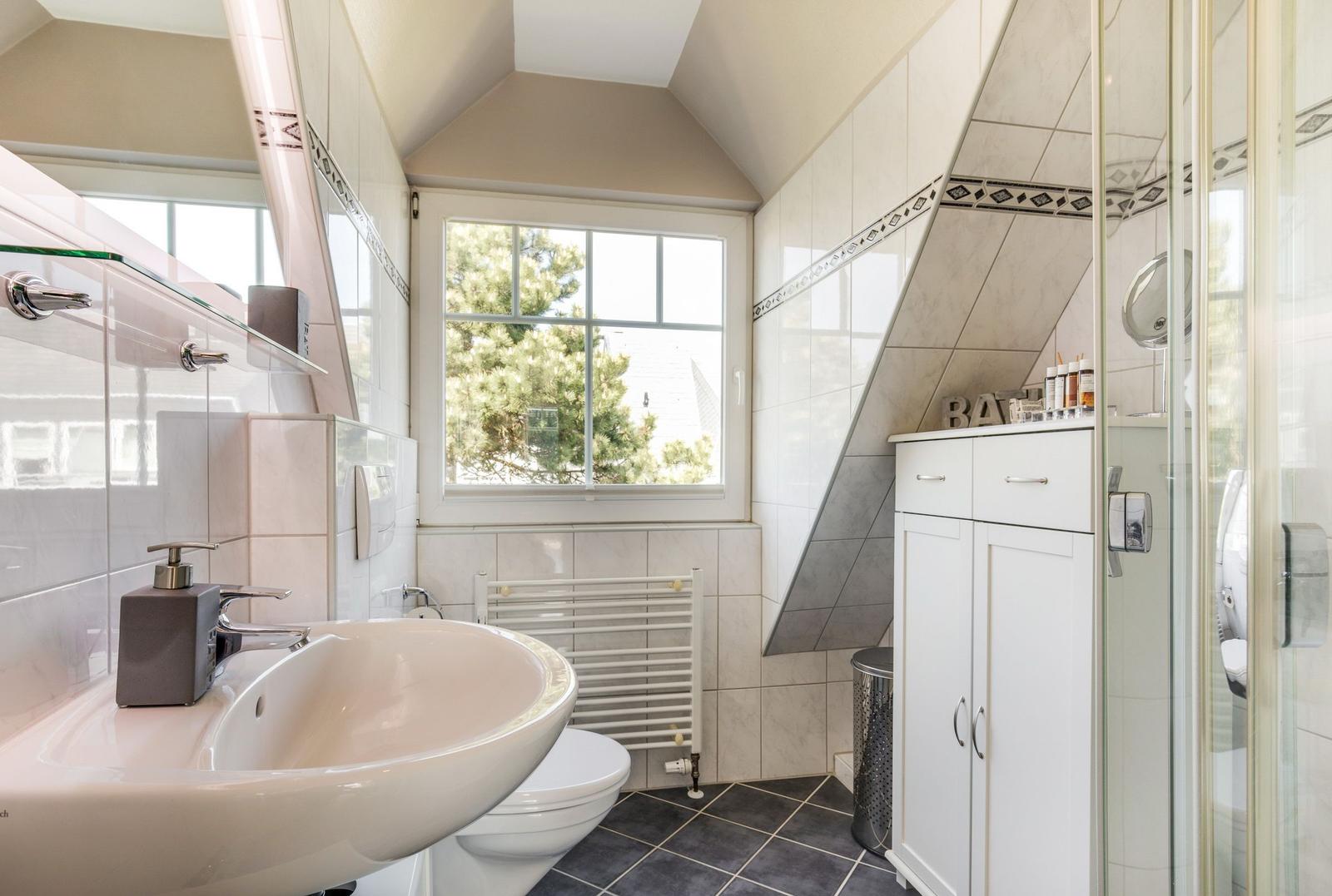 Badezimmer mit Dusche, Waschbecken und Fenster. Fliesen und weiße Möbel.
