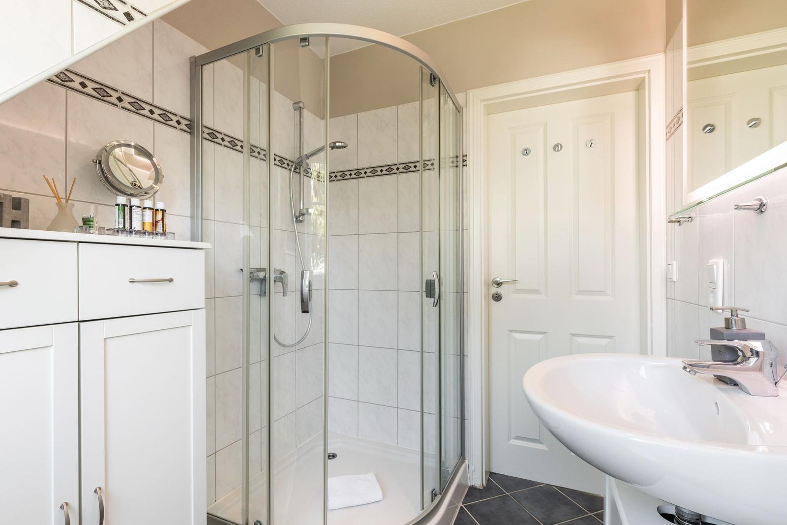 Badezimmer mit Dusche, Waschbecken und Spiegel.