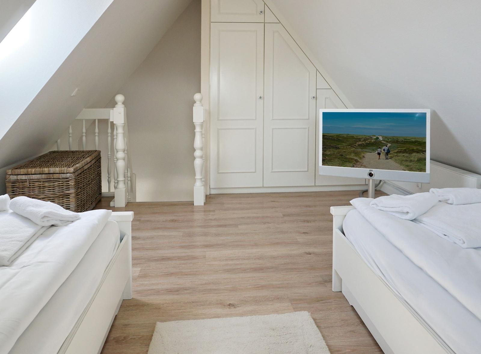 Zimmer mit zwei Betten, Schrank und Fernseher unter Dachschrägen.