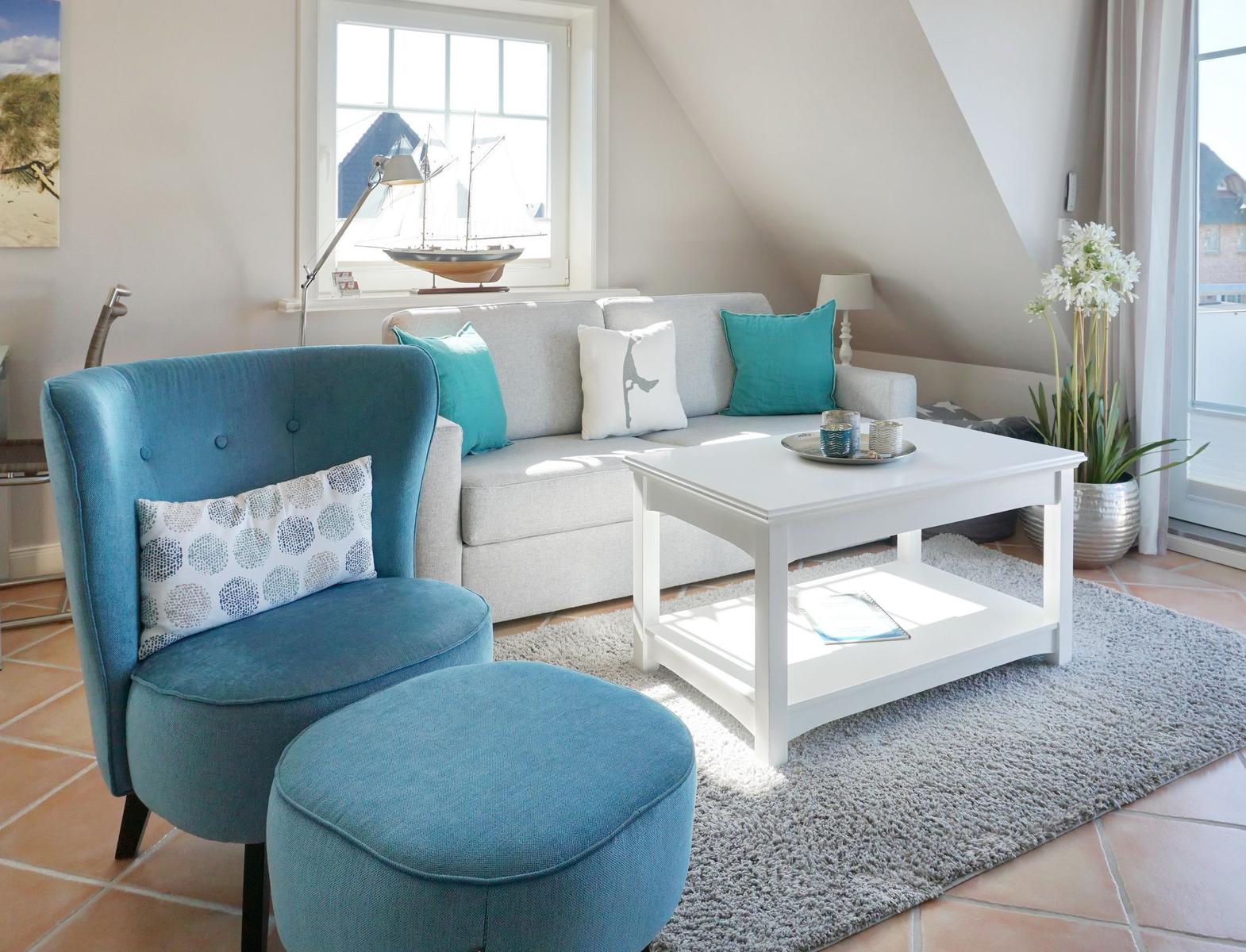 Ein Wohnzimmer mit blauem Sessel, grauem Sofa und weißem Couchtisch.