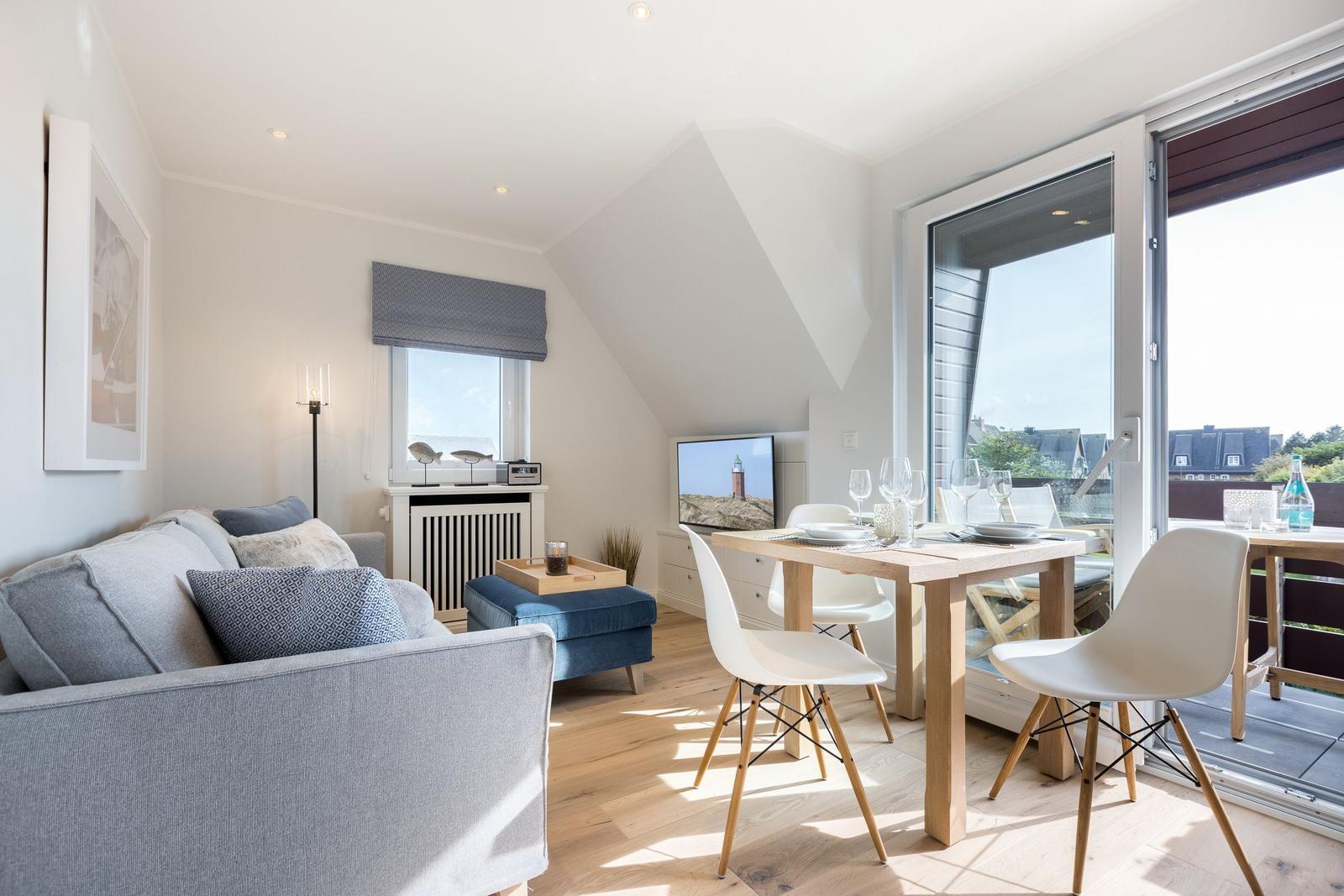 Wohn- und Essbereich mit Sofa, Tisch und Stühlen. Glastür führt auf Balkon mit Blick.