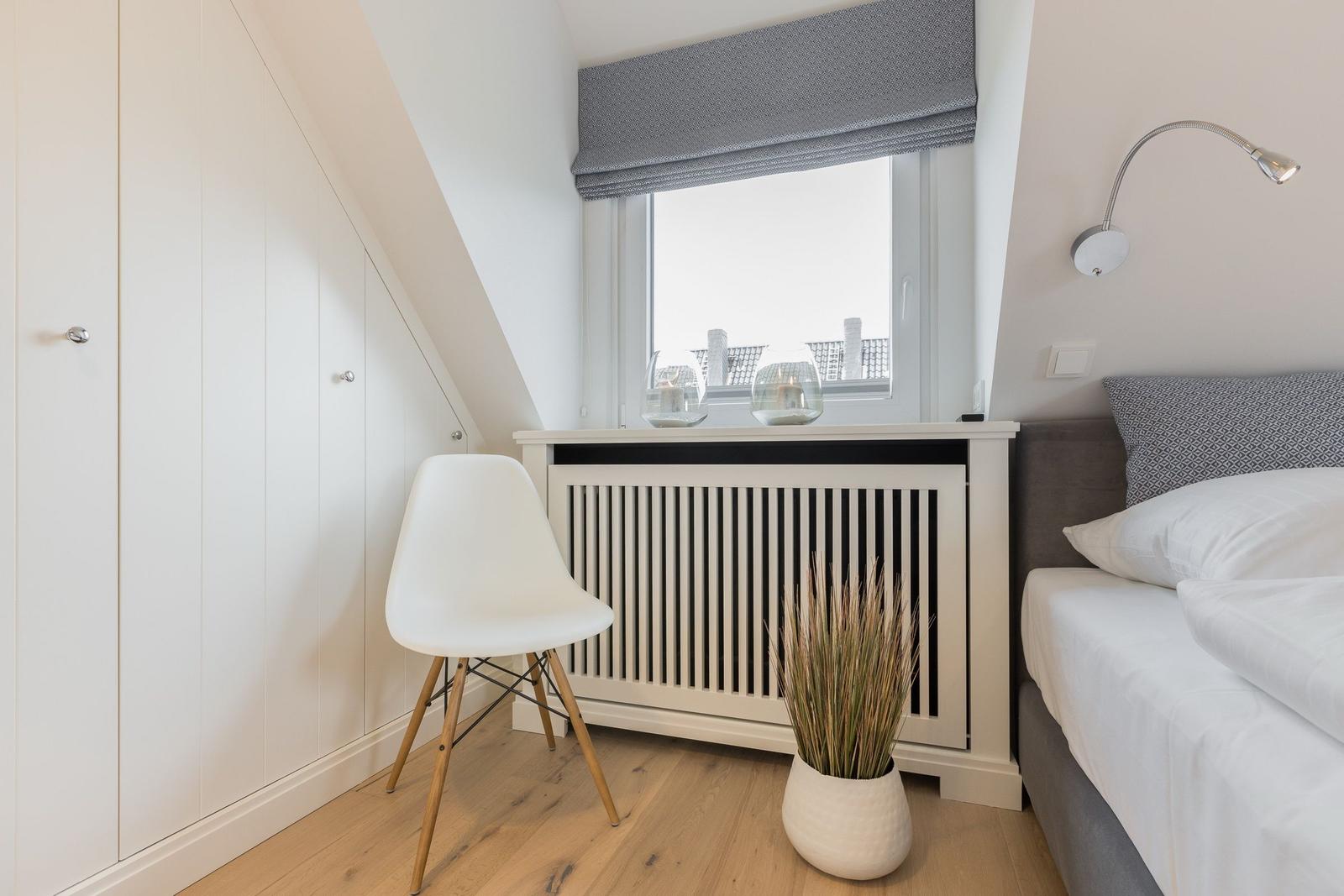 Schlafzimmer mit Bett, Stuhl und Fenster unter Dachschräge.