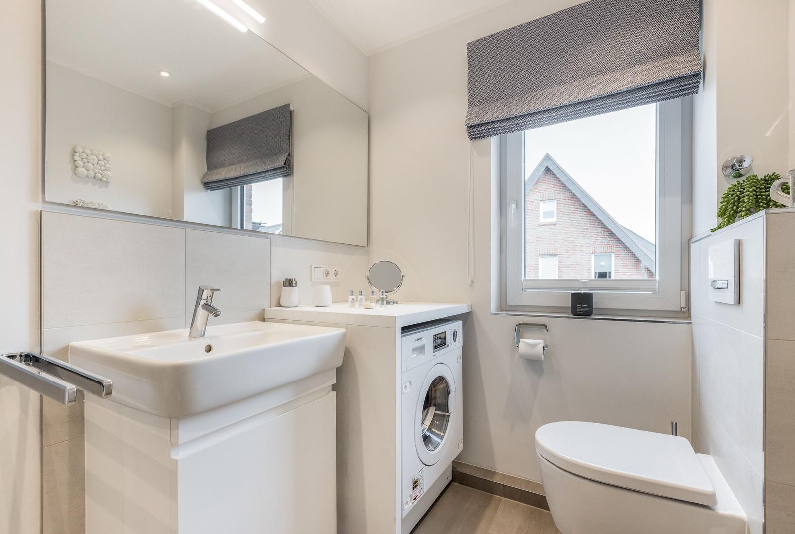 Badezimmer mit Waschmaschine, Spiegel und Toilette. Fenster mit Rollladen.
