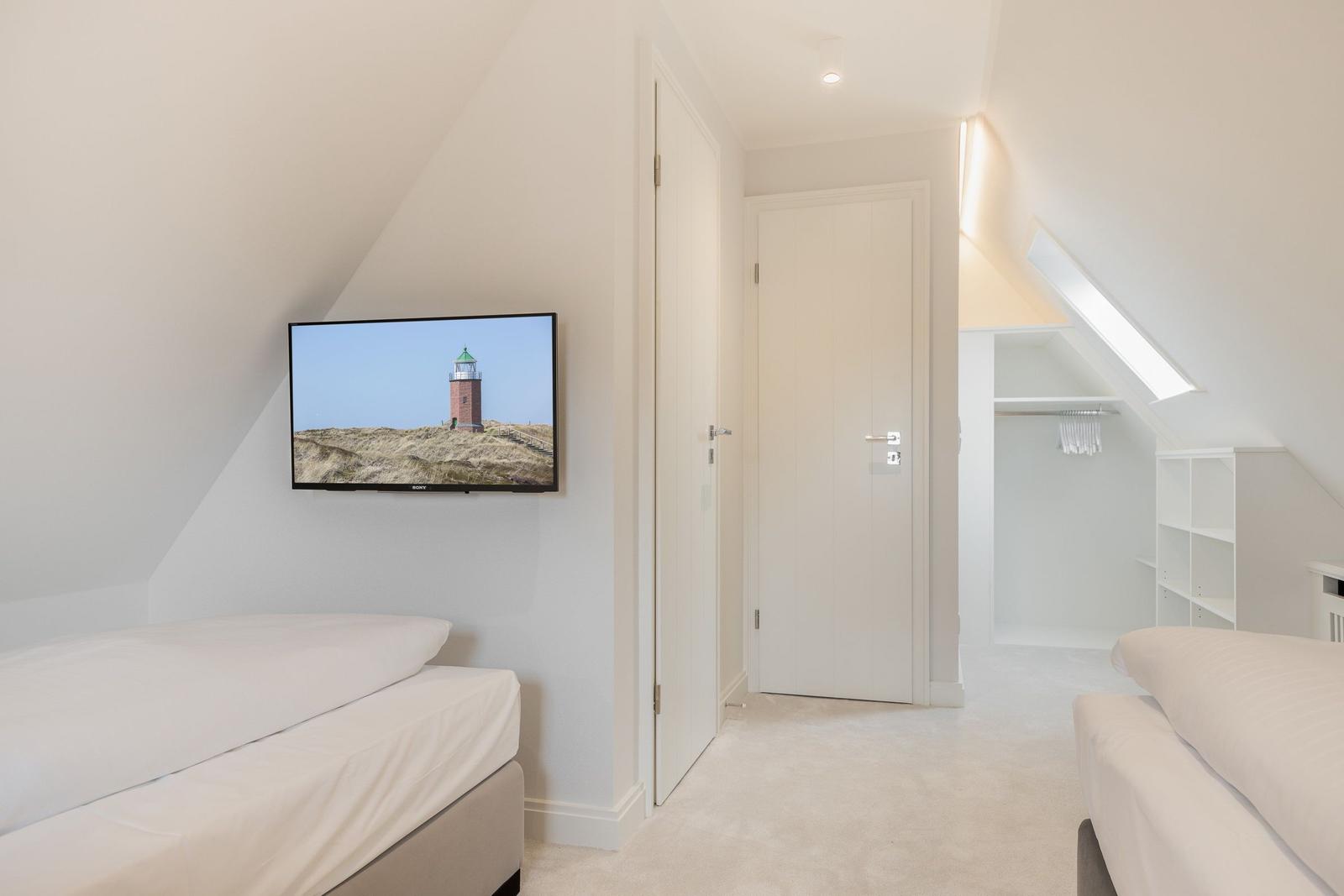 Zwei Betten, TV mit Leuchtturm-Bild, Kleiderschrank und Dachschrägen.