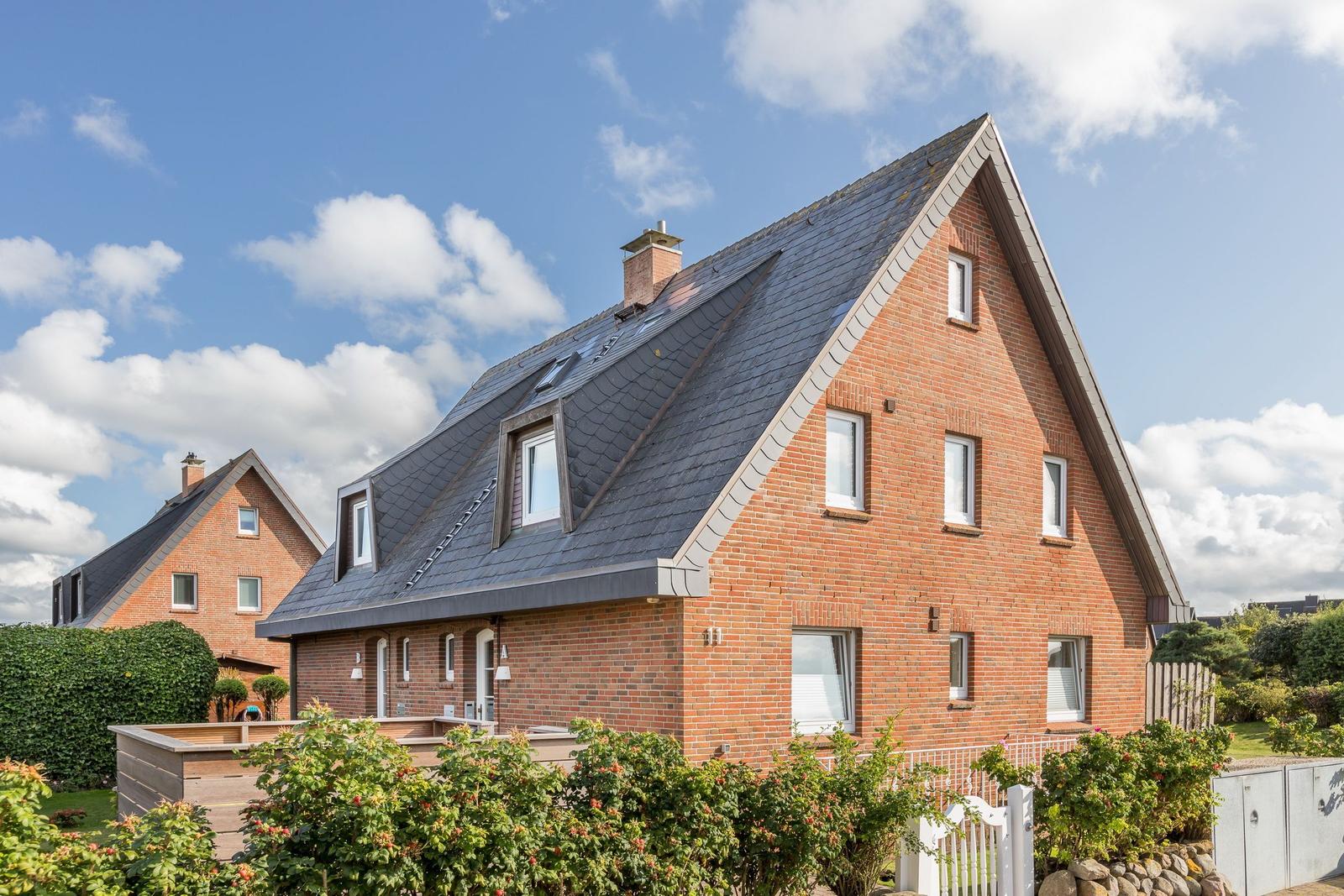 Zweistöckiges Haus mit rotem Backstein und dunklem Dach unter blauem Himmel.