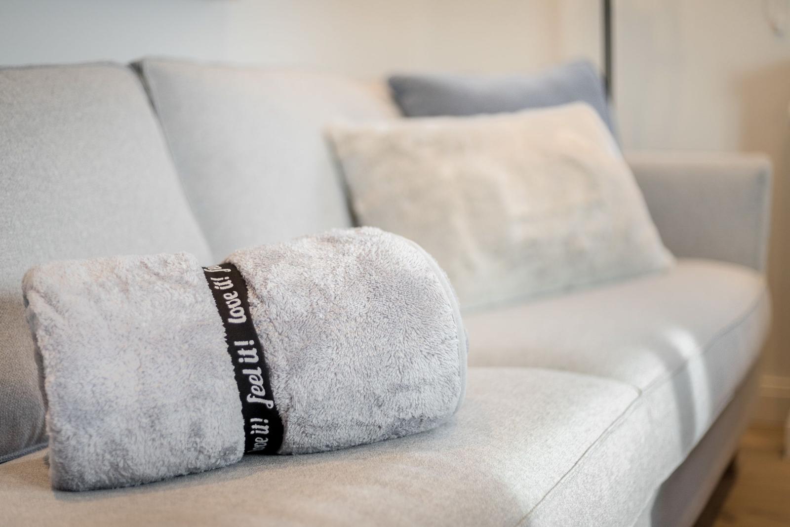 Graue Couch mit Kissen und einem gefalteten Handtuch.