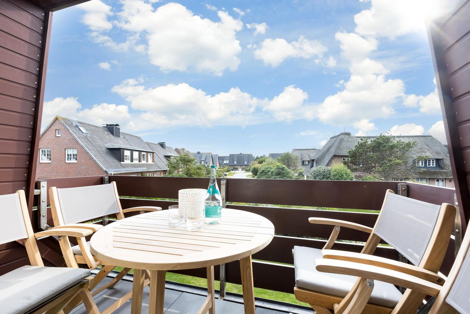 Terrasse mit Tisch und Stühlen, Blick auf Dächer und Grünflächen unter blauem Himmel.