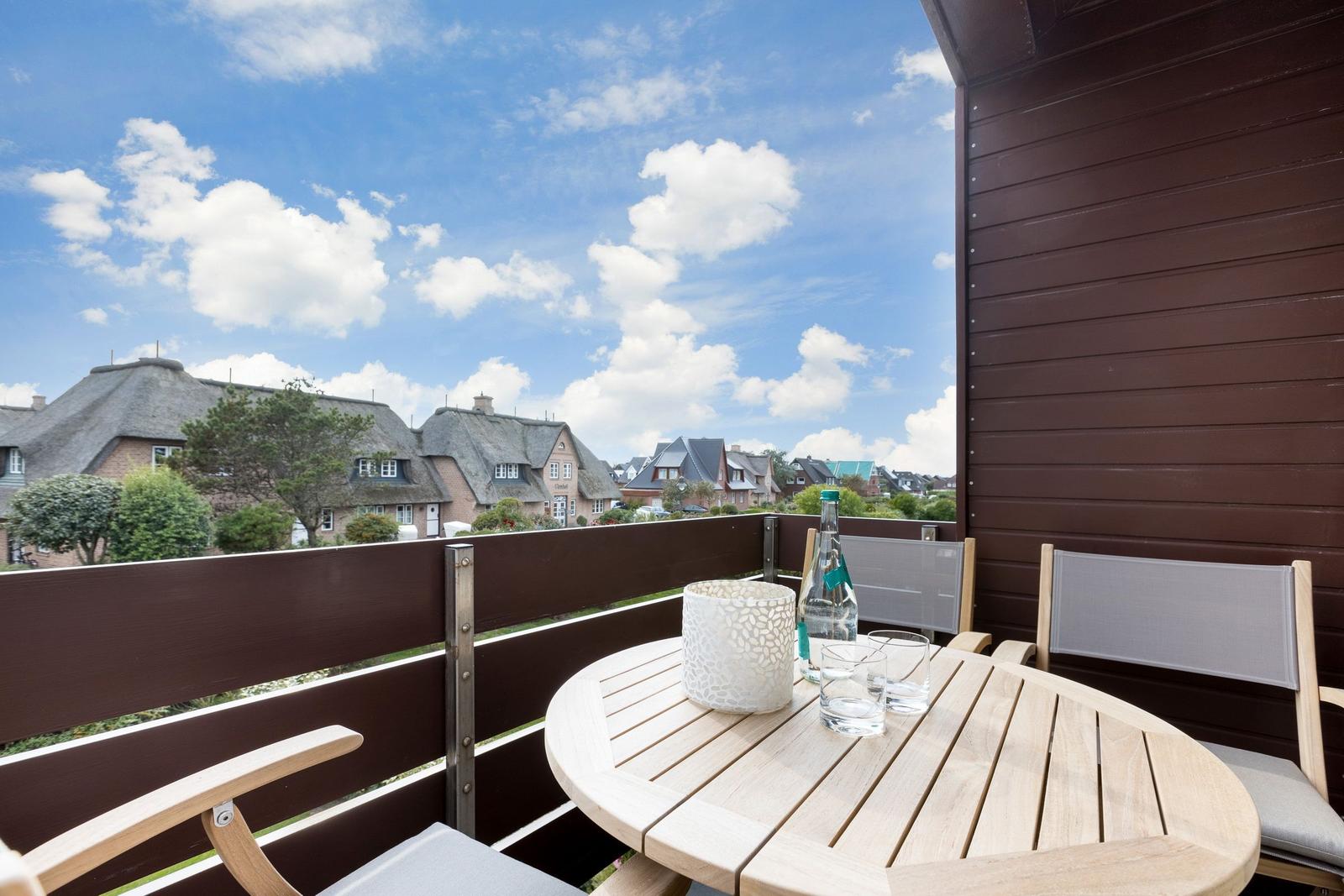 Terrasse mit Tisch und Stühlen, Blick auf Dächer und Himmel.