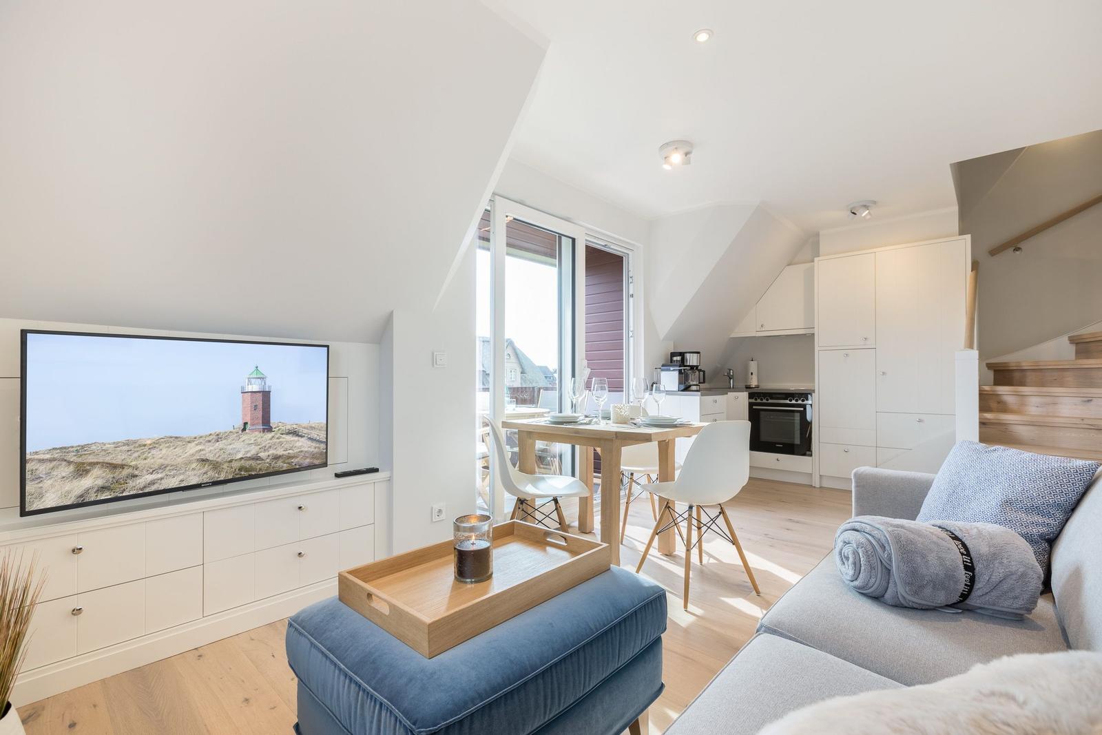 Wohn- und Essbereich mit TV, Sofa und Küche. Fenster zur Terrasse.