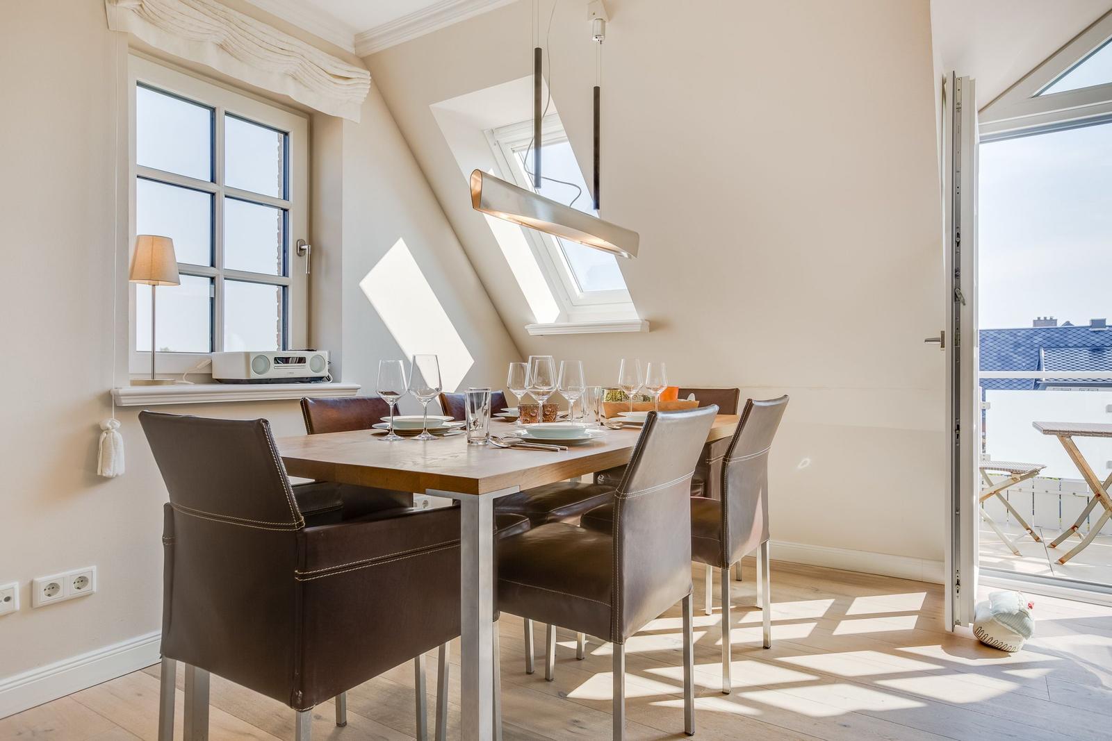 Esszimmer mit Tisch, Stühlen und Fenster. Dachfenster und Balkontür sichtbar.