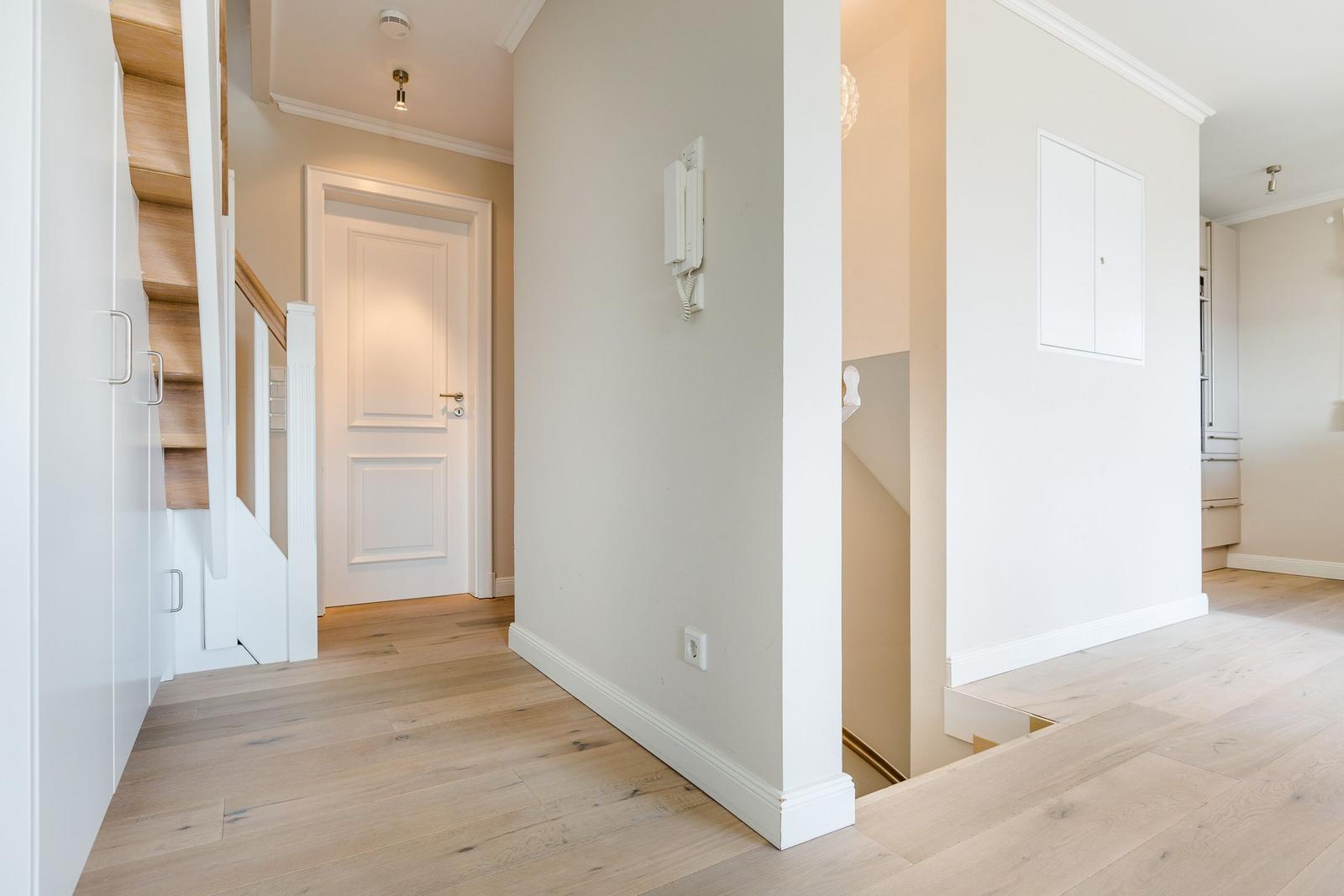 Hausflur mit Holzboden, weißen Wänden und Treppe zur oberen Etage.