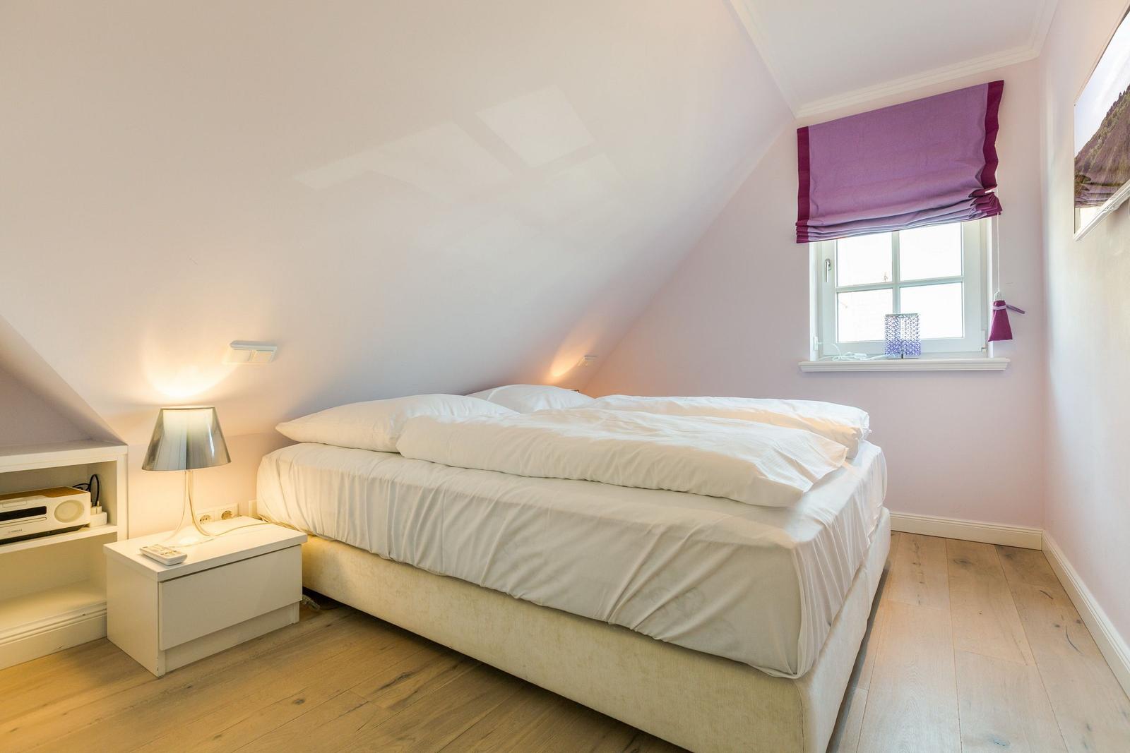 Schlafzimmer mit Doppelbett, Fenster und Nachttisch.