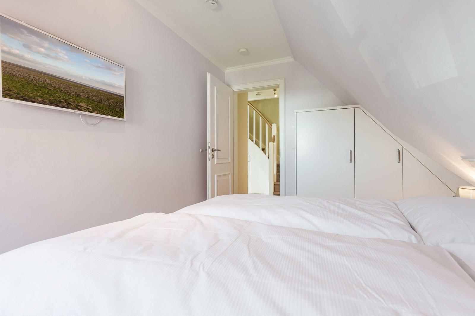 Schlafzimmer mit Dachschrägen, Bett, Kleiderschrank und Fernseher an der Wand.