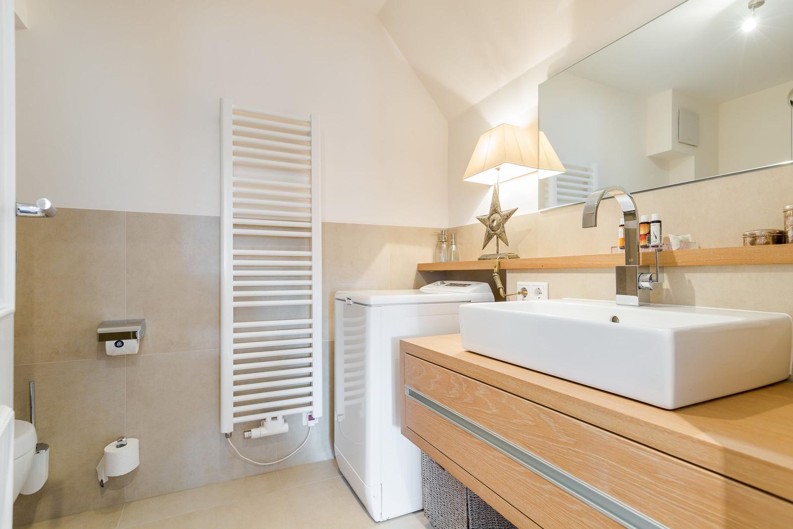 Badezimmer mit Waschmaschine, Spiegel und Waschbecken auf Holzunterschrank.