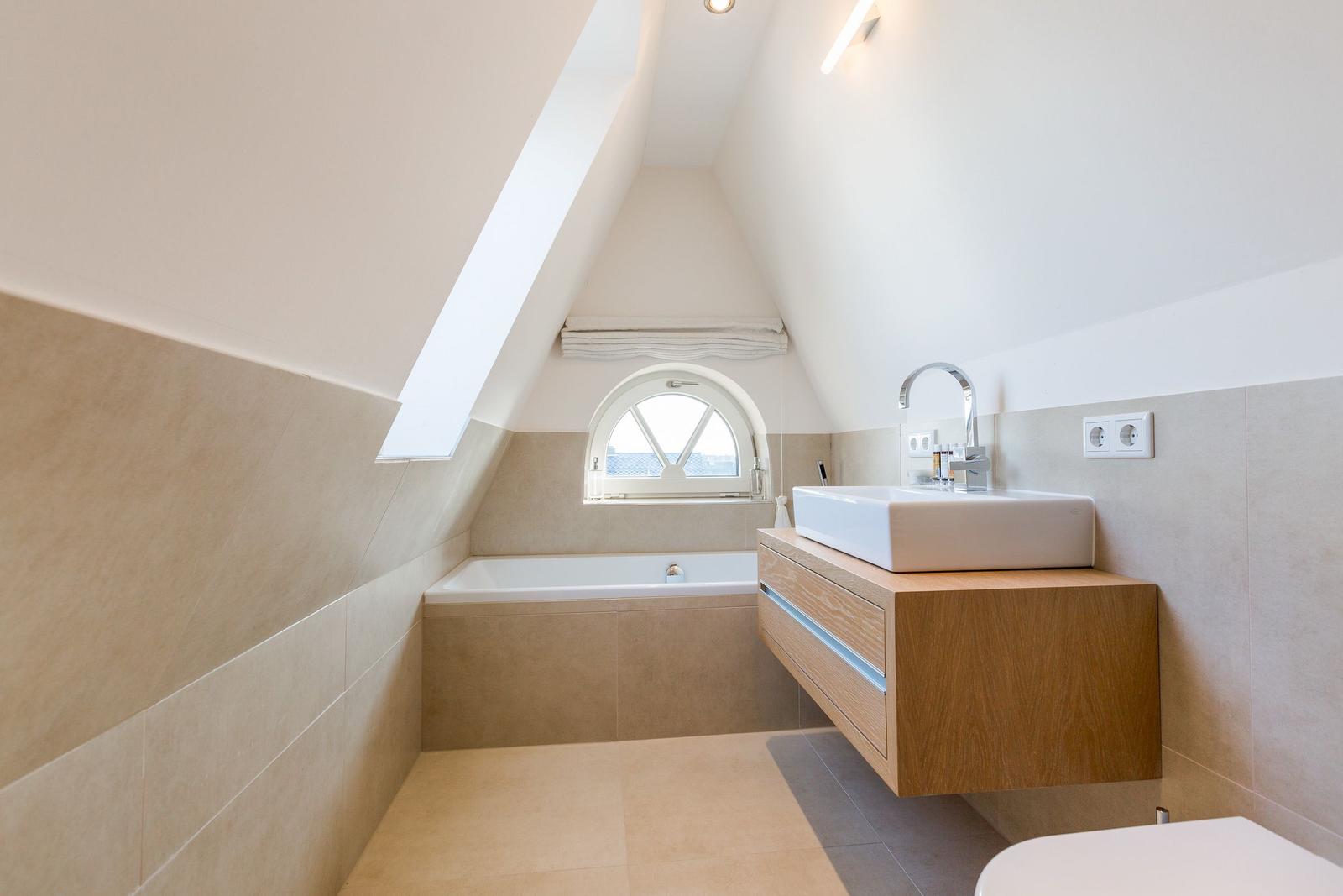 Badezimmer mit Badewanne, Waschtisch und Dachfenster.