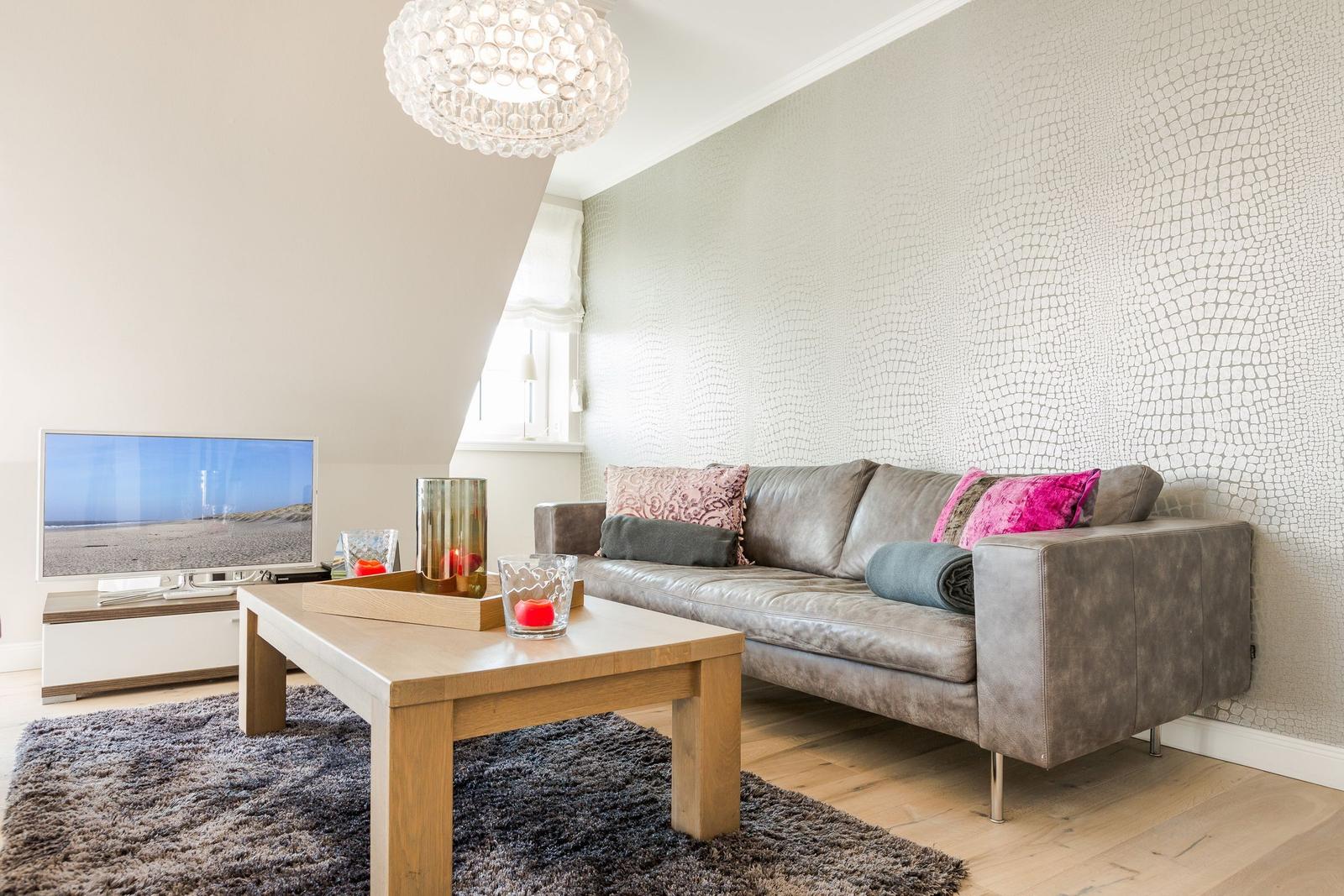 Wohnzimmer mit Sofa, Couchtisch und Fernseher. Wand mit Mosaikoptik.