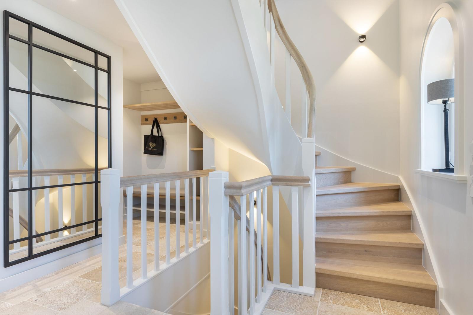 Light staircase with wooden steps and white balustrade. Left glass wall, right window with lamp.