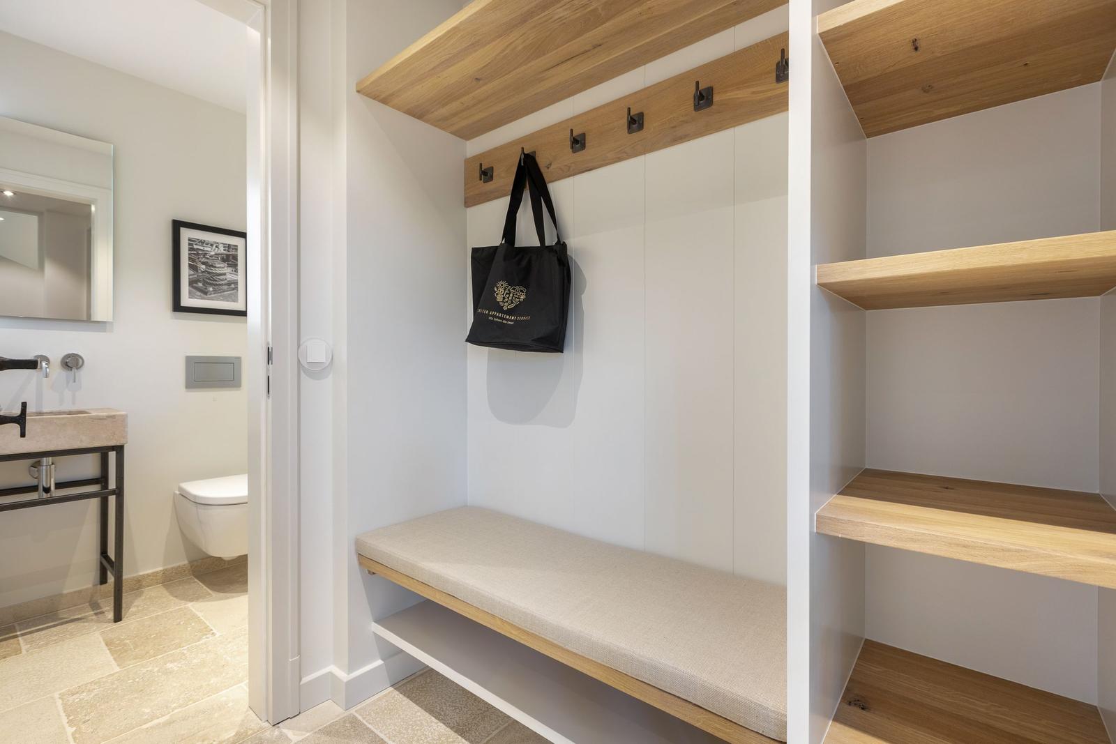Entry area with bench, hooks, and shelves. Toilet and sink in the background.