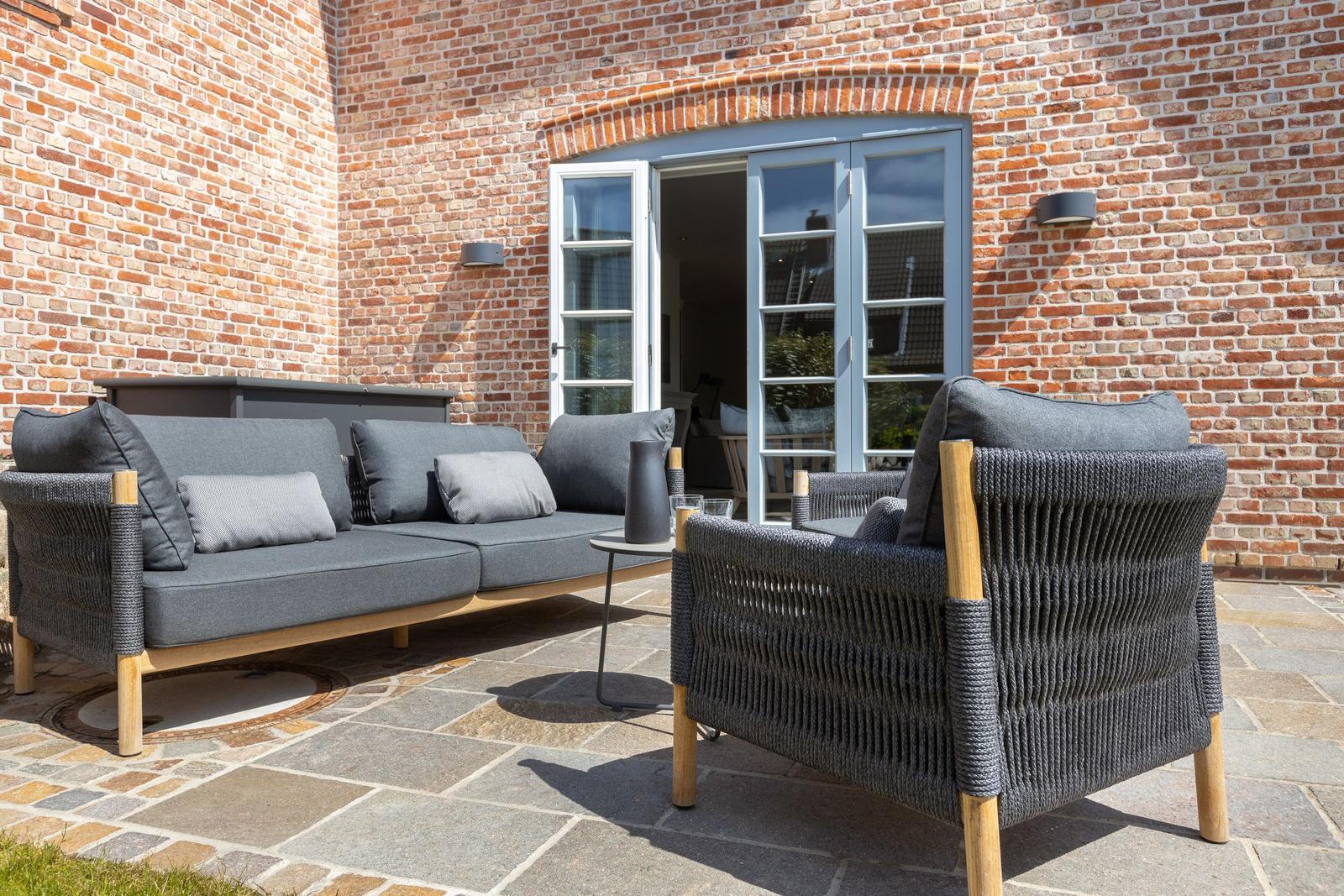 Terrace with gray sofa and chair in front of brick wall and glass door.