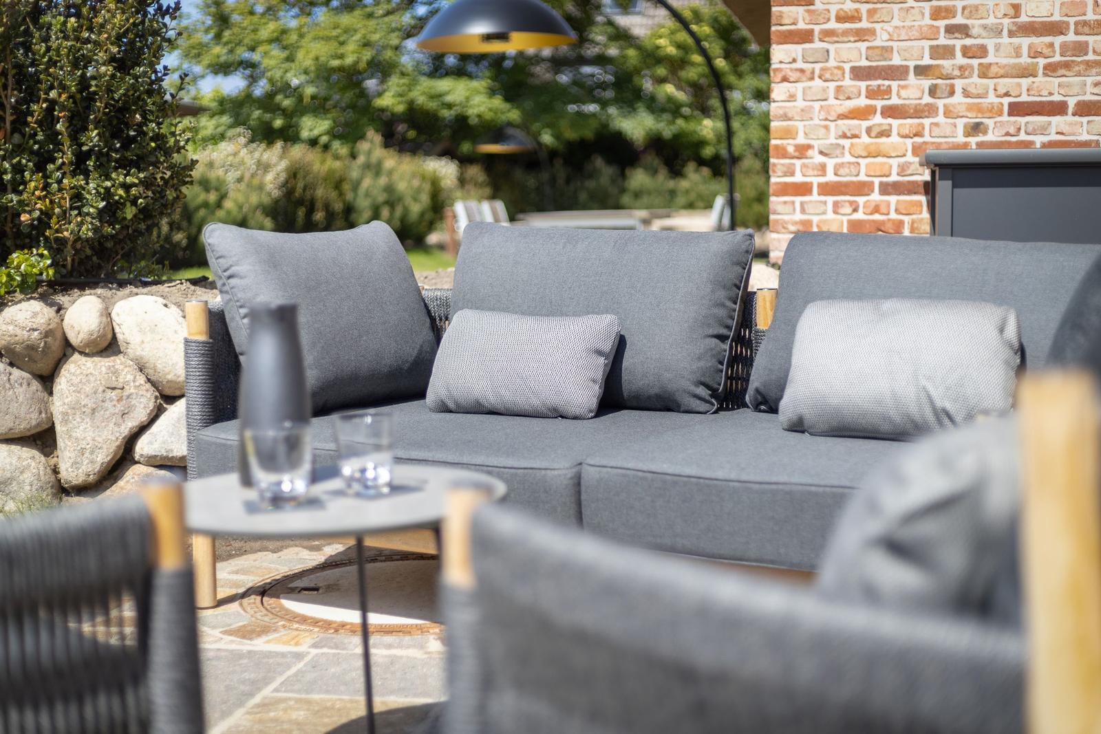 Outdoor area with gray sofa, table, and stone seating surface. Background with stone wall and trees.