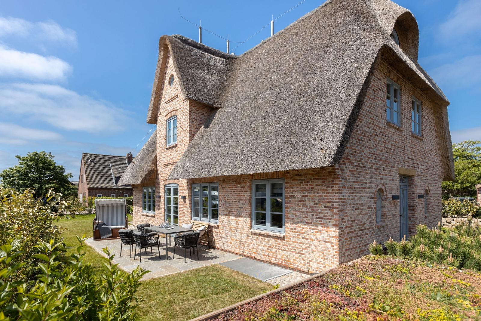 House with thatched roof and garden area with table and chairs.