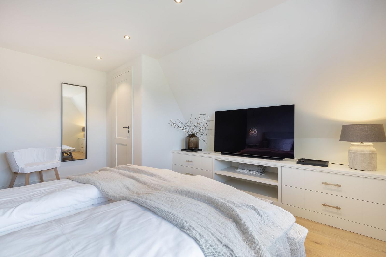 Bedroom with bed, TV, and dresser. Mirror and chair are visible.