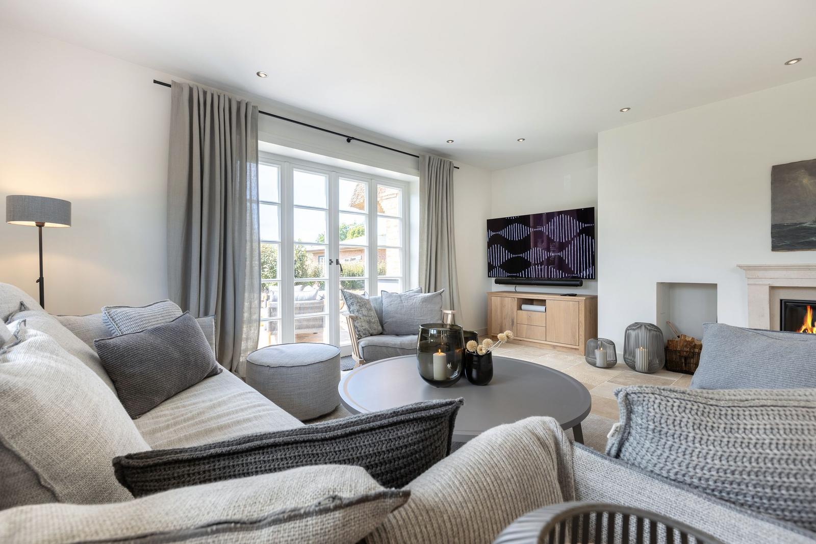 Living room with sofa, TV, and fireplace. Windows overlook the garden.