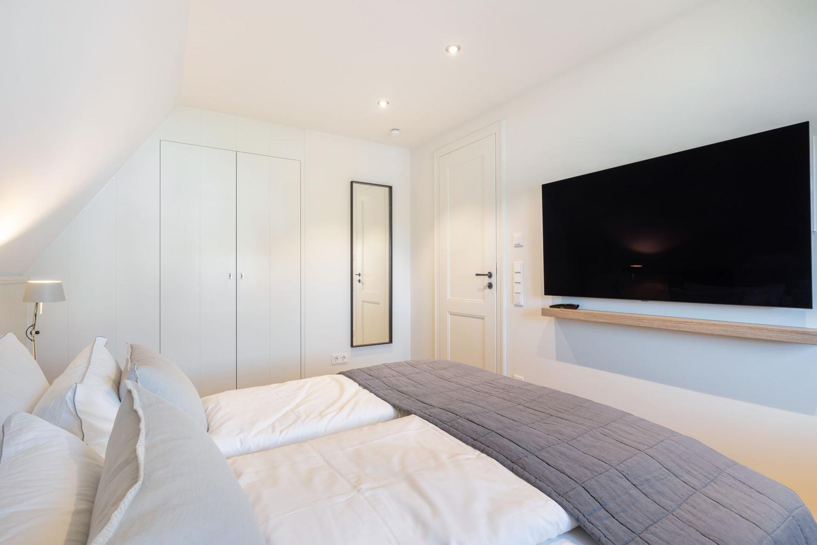 Bedroom with double bed, wardrobe, mirror, and wall-mounted TV.