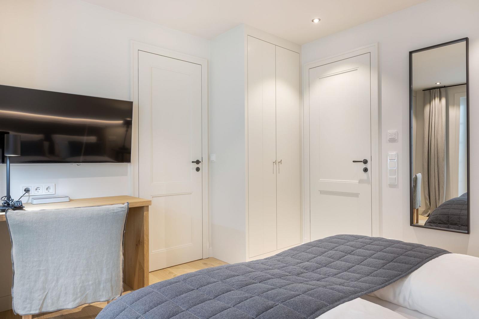 Bedroom with bed, wardrobe, mirror, and desk with TV.